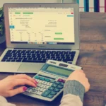 Person using a calculator and laptop to plan a monthly budget