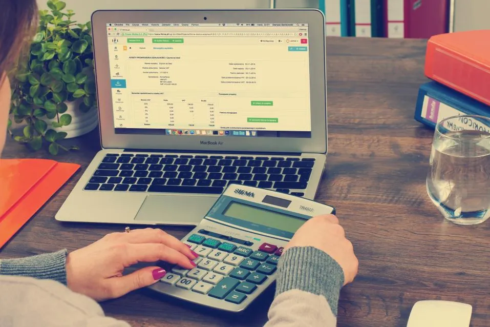 Person using a calculator and laptop to plan a monthly budget