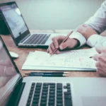 Professionals using laptops and AI tools at a shared work desk